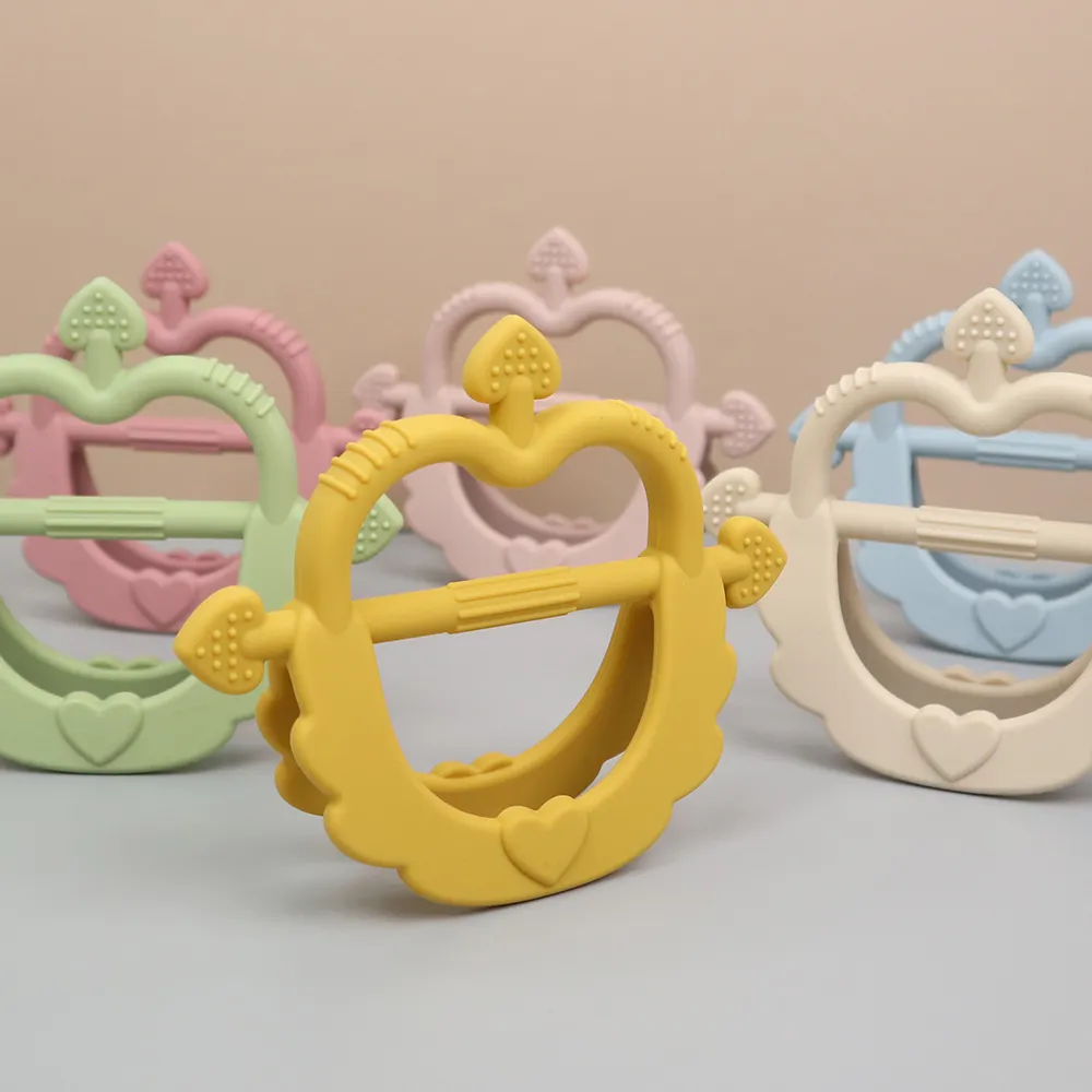 Lifestyle lineup of Cupid Heart Handle Teethers in mango, olive, rose pink, dusty blue and beige, soft silicone with easy-grip arrow bar.